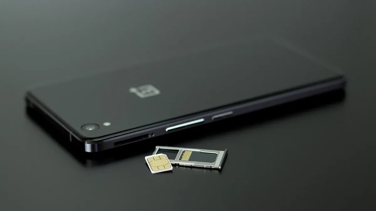 A black smartphone lying on its side with two SIM cards in front of it.